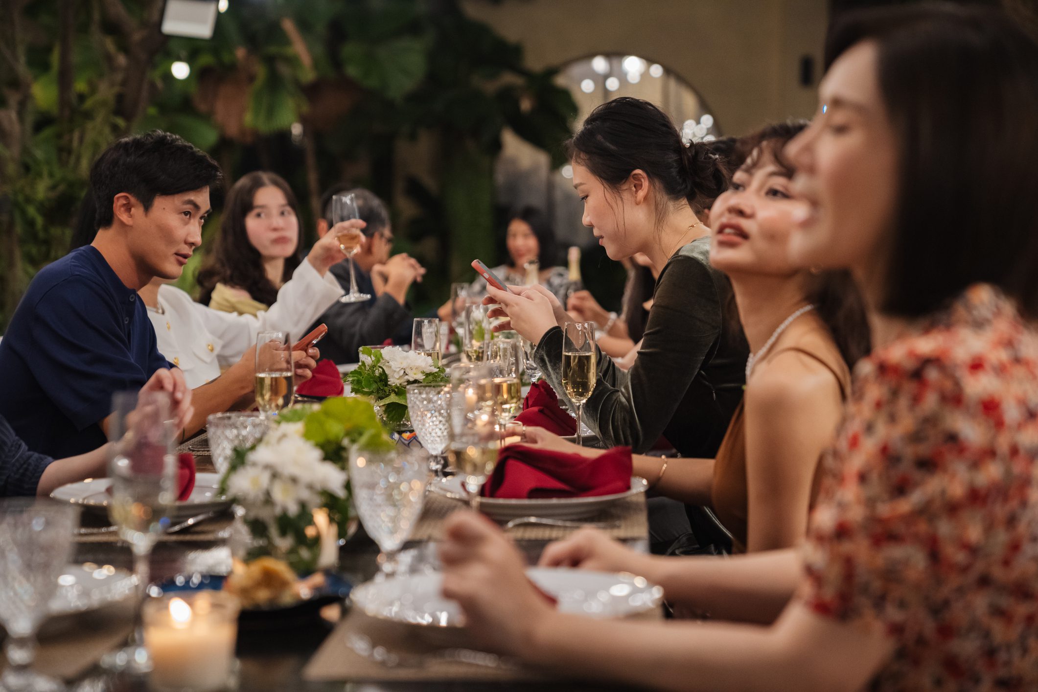 A large family enjoying dinner together at a long table in an elegant outdoor setting, sharing conversation and a meal in a warm evening atmosphere.
